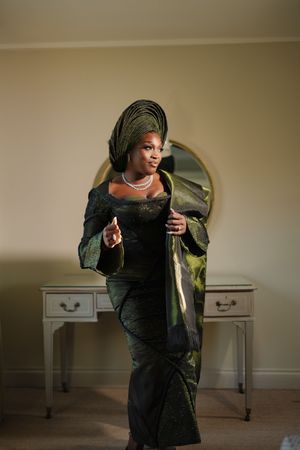 Elegant dark green and black traditional Nigerian attire with gele headwrap photographed in front of a vanity table.