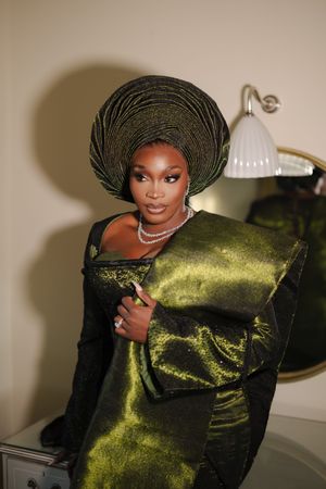 Elegant portrait featuring a woman in a dark green velvet gown and traditional gele headpiece against a neutral background.