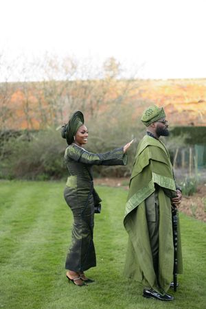 Couple in matching olive green traditional African attire posing together on a grassy lawn.