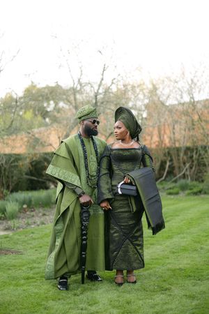 African couple in coordinated green formal attire posing together outdoors.