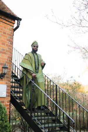 Individual in olive green cape and sunglasses poses on brick staircase at dusk.