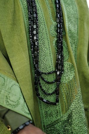 Close-up detail of green fabric with black beaded necklace and intricate embroidered patterns.