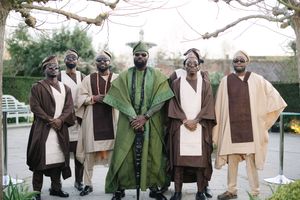 A group of men dressed in traditional West African agbada and formal robes standing together outdoors.