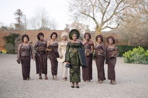 Group photo of people wearing coordinated brown and green traditional African formal wear outdoors.