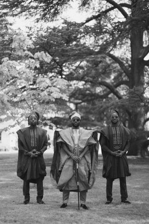 Black and white photo of three men in traditional African ceremonial robes standing in a garden.