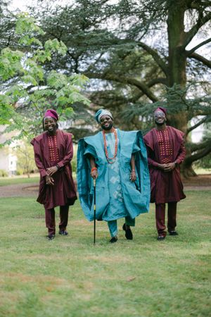 Three figures in coordinated African attire walk together through a garden setting.