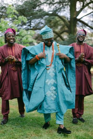 Three people in traditional African clothing share a joyful moment wearing coordinated agbada robes.