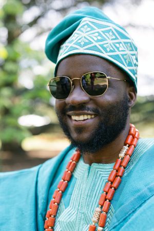Close-up portrait showing traditional African headwear with geometric patterns, coral beads and sunglasses.