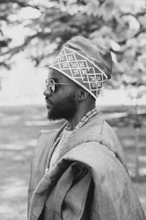 Side profile shot showing geometric patterned headwear and traditional African attire in black and white.