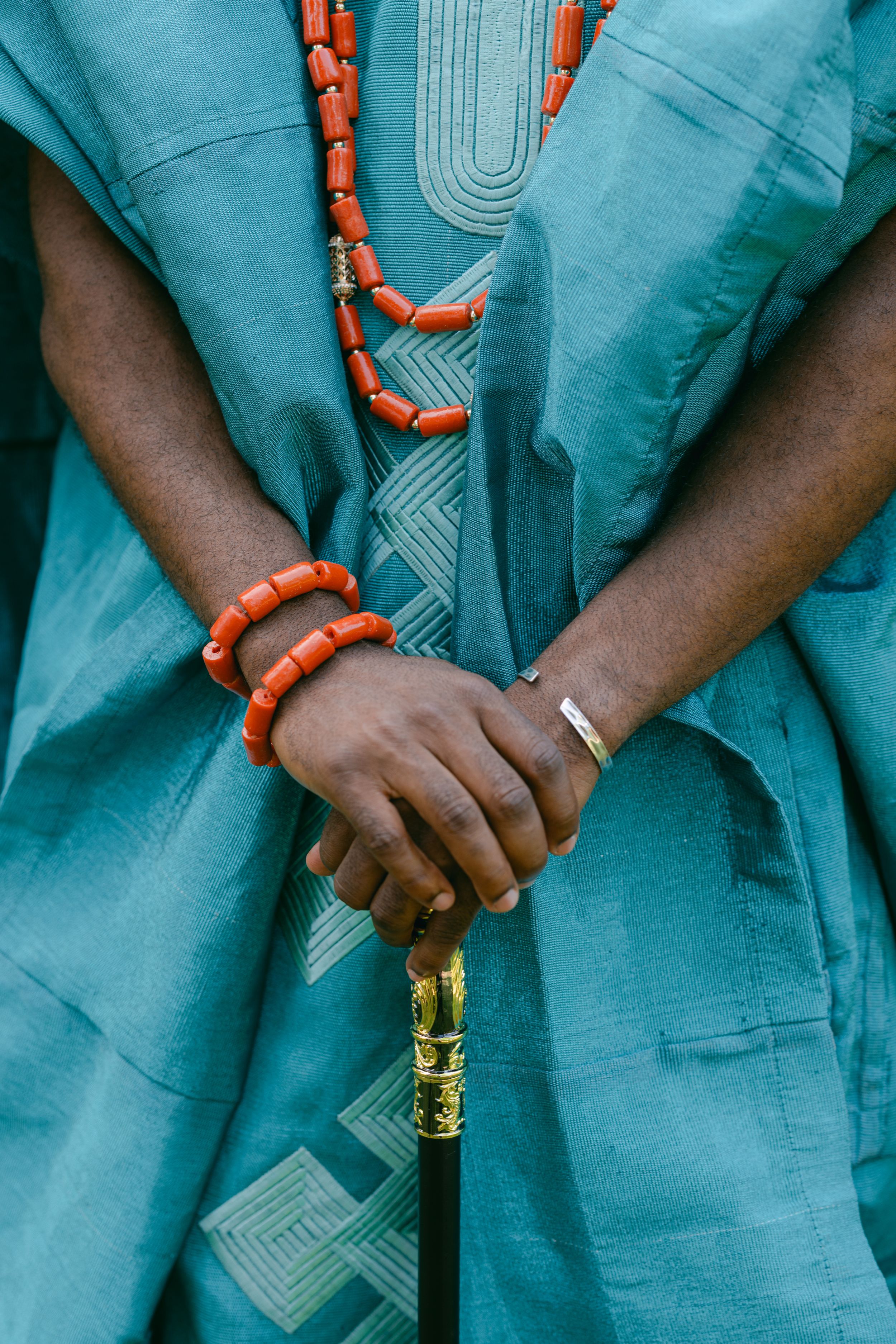 Detail shot of hands holding cane with coral bead bracelets and turquoise embroidered traditional garment.