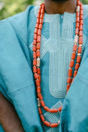 Close-up of coral beaded necklace against turquoise embroidered traditional African clothing.
