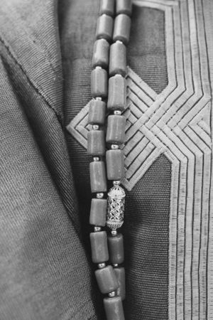 Black and white detail of beaded necklace against geometric embroidered pattern on traditional garment.