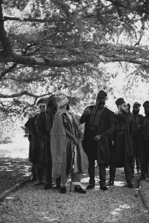 A black and white photo shows wedding guests in traditional attire gathered beneath trees.