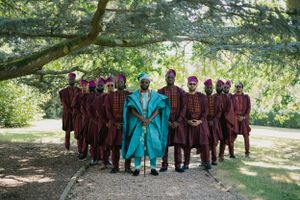 Group photo showing contrast of burgundy and turquoise traditional African attire under trees.