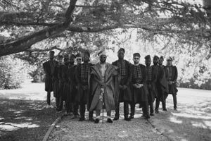 Black and white photograph of wedding attendees in formal attire standing together under trees.
