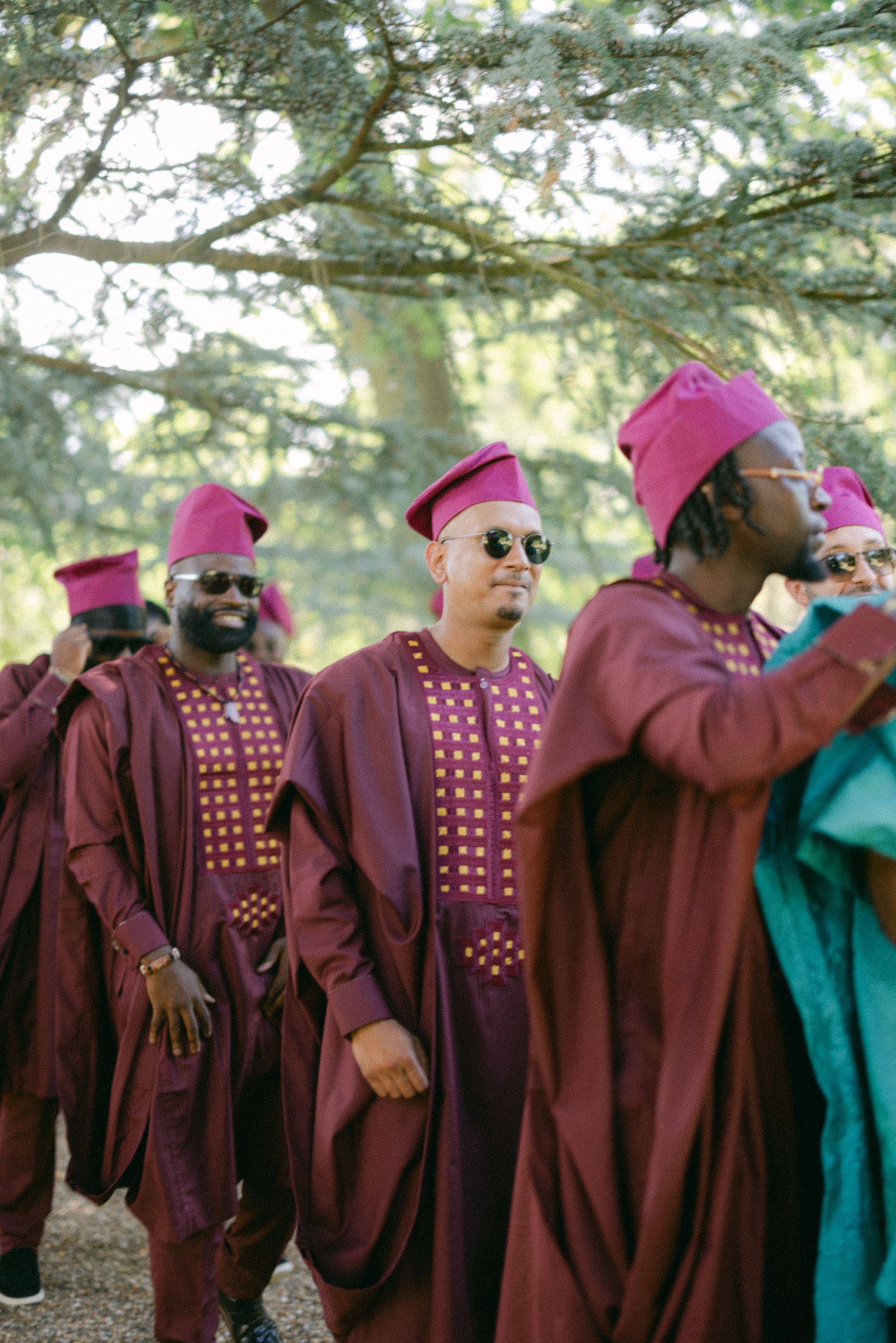 Line of people wearing coordinated burgundy traditional outfits with pink caps in outdoor setting.