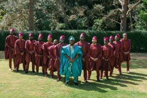 A choir group in burgundy robes stands behind their conductor in bright turquoise attire.