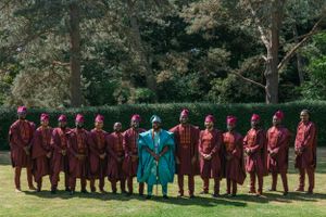 Formal group photo of a choir wearing burgundy robes with conductor in turquoise on grass.