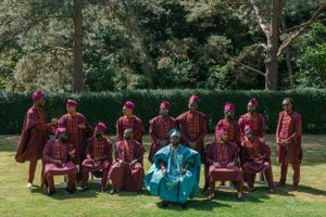 Group photo showing traditional African wedding party in burgundy attire with central figure in turquoise.