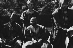 Vintage black and white photograph of performers in patterned clothing gathered outdoors.