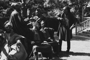 Historical black and white image of people in traditional dress conversing outdoors.