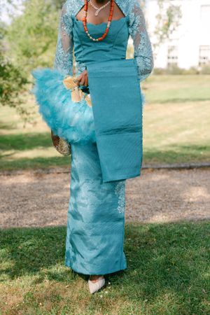 Full-length view of turquoise traditional dress with lace details and tulle handbag.