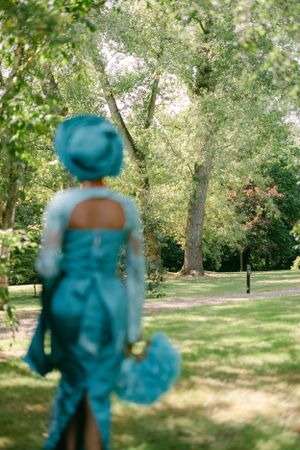 Back view of person in turquoise dress standing in sunny garden setting.