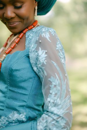 Close-up detail of turquoise dress with delicate lace sleeve and coral beaded necklace.