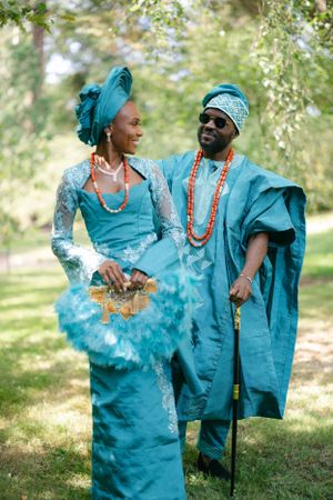 Happy couple in traditional turquoise Nigerian attire with beaded necklaces pose together in a garden setting.