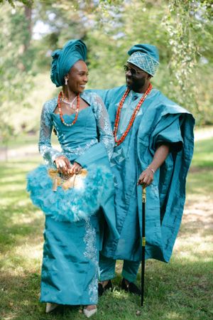 Couple wearing matching teal traditional African outfits share a joyful moment outdoors.