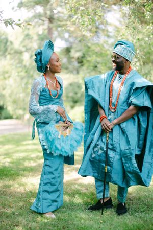 Couple in coordinated turquoise traditional Nigerian outfits engage in conversation outdoors.