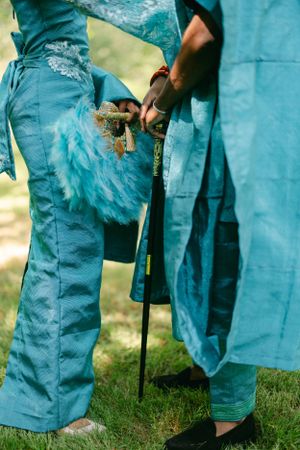Close-up detail of traditional blue African clothing and walking stick against green grass.