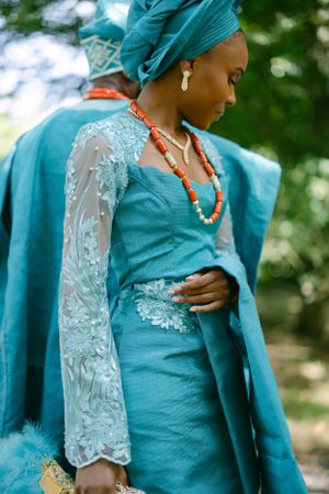 Detail shot of turquoise gown with lace sleeves and coral beaded necklace in outdoor setting.