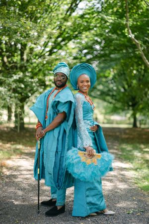 A couple in coordinating turquoise traditional Nigerian attire pose together on a wooded path.