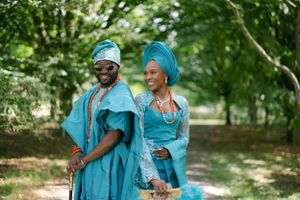 A couple wearing coordinated blue Nigerian outfits share a joyful moment outdoors.