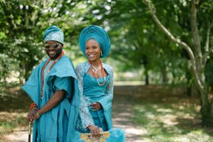 A couple in traditional Nigerian attire smile and pose together in a park.
