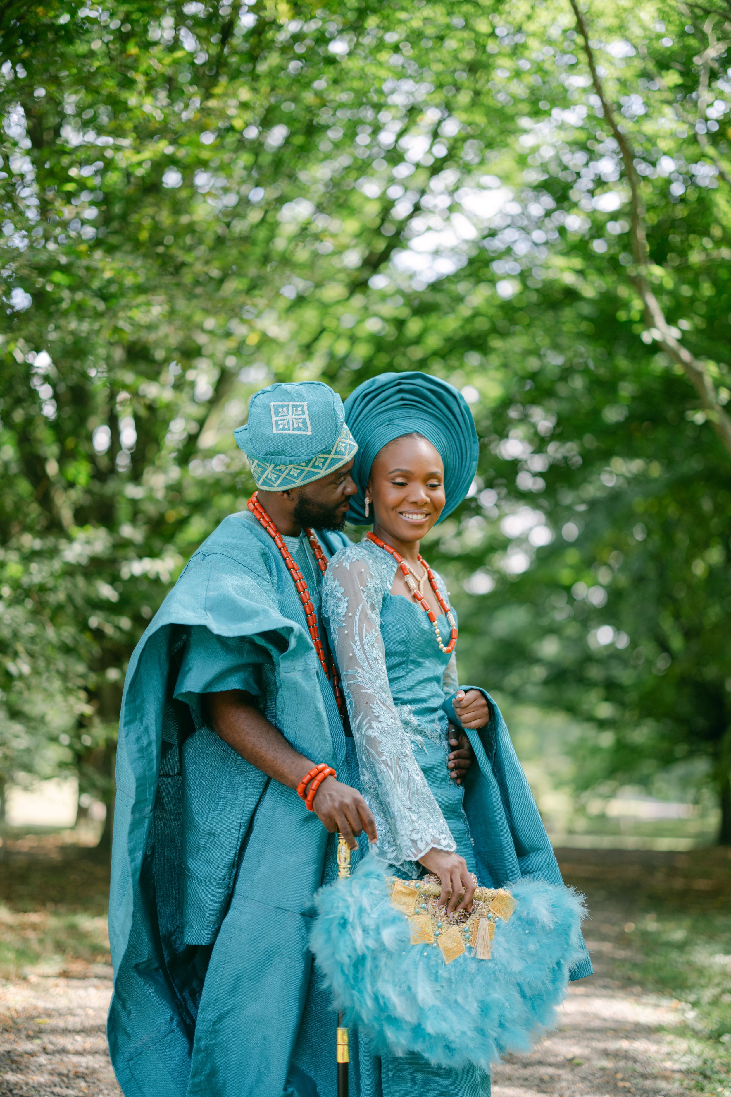 A couple in matching teal traditional Nigerian outfits dance together in a wooded setting.