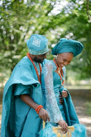 A couple in coordinated turquoise Nigerian attire share a joyful moment in a park.