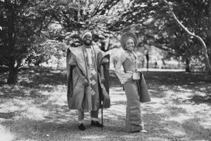 A black and white photo of a couple in traditional African attire standing in a park.