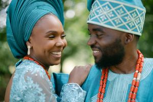 A couple in traditional teal Nigerian attire share a joyful moment outdoors.