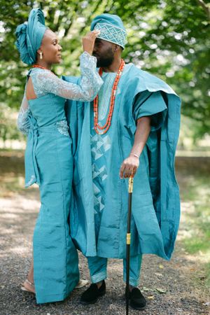 Couple wearing coordinated turquoise Nigerian wedding outfits posing together outdoors.
