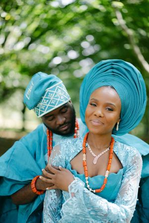 Traditional wedding couple in matching teal outfits with coral beaded accessories.