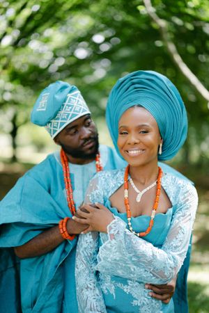 Couple in traditional African attire embrace while smiling outdoors.