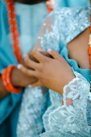 Detail shot of hands and lace fabric in teal and coral traditional wedding attire.