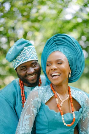 Joyful couple in matching turquoise traditional Nigerian attire sharing a happy moment outdoors.