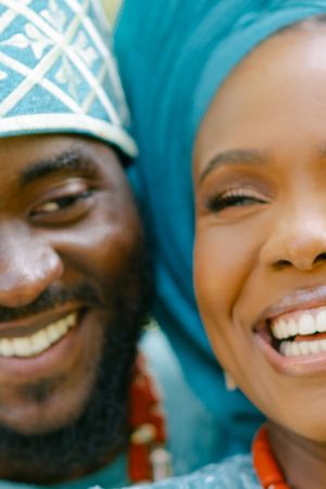 Close-up portrait of a couple wearing traditional Nigerian clothing and headpieces in vibrant turquoise.