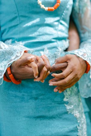 Close-up of hands with coral bracelets against turquoise traditional lace clothing.