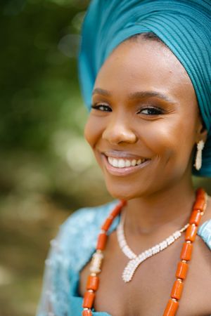 Close-up portrait showing traditional turquoise gele headwrap and coral beaded jewelry.