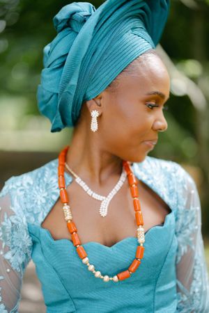 Side profile showing intricate details of turquoise gele headwrap and beaded jewelry.