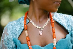 Close-up detail of coral beaded necklace and pearl jewelry against turquoise traditional attire.